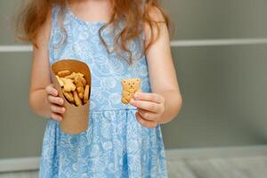 feliz pequeno menina segurando Fora uma papel copo com caseiro encaracolado biscoitos, escola refeições foto