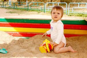 bebê menina jogando dentro a caixa de areia em a Parque infantil em uma verão ensolarado dia foto