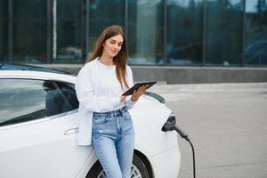 elétrico carro cobrando dentro rua. ecológico carro conectado e cobrando baterias. menina esperando poder fornecem conectar para elétrico veículos para carregando. foto