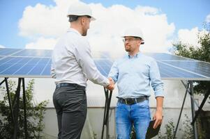 trabalhadores tremendo mãos em uma fundo do solar painéis em solar poder plantar foto