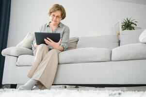 Senior mulher usando digital tábua dentro vivo quarto às casa foto