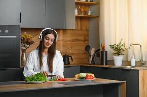 feliz sorridente fofa mulher é preparando uma fresco saudável vegano salada com muitos legumes dentro a cozinha às casa e tentando uma Novo receita foto