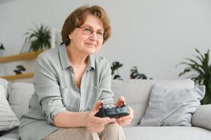 uma altamente emocional Mais velho senhora senta em a sofá às casa e tocam vídeo jogos. Avó vitórias enquanto sentado sozinho às lar. foto