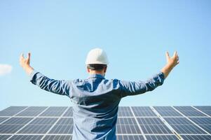 feliz trabalhando solar estação levantando dele mãos em uma fundo do fotovoltaico painéis. Ciência solar energia foto
