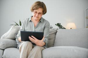 Senior mulher usando digital tábua dentro vivo quarto às casa foto