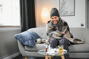 uma doente homem senta às casa em uma cinzento sofá com uma cobertor. doença, proteção, coronavírus, doença, gripe foto