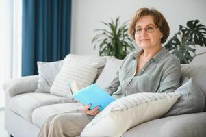 retrato do atraente focado alegre mulher sentado em divã lendo livro passatempo sonhar Acordado às casa casa plano interior. foto