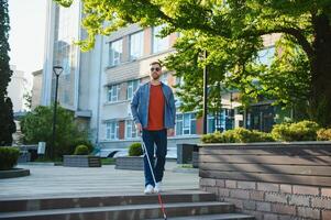 jovem bonito cego homem caminhando com bastão dentro Cidade foto