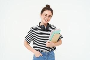 jovem mulher com cadernos, livros e estude material, posando sobre branco fundo, desgasta fones de ouvido sobre pescoço foto