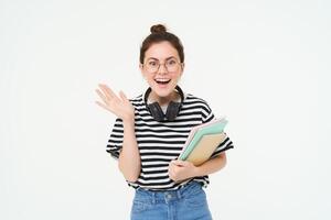 retrato do animado jovem mulher dentro copos, parece surpreso e feliz. aluna em pé em branco fundo com livros e cadernos foto