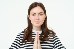 retrato do jovem mulher expressa dela gratidão, mostra obrigado você, namaste gesto, segurando mãos apertado juntos perto peito e sorridente, em pé sobre branco fundo foto