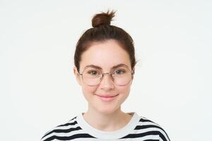 fechar acima retrato do fofa jovem mulher dentro copos, olhando às Câmera e sorridente, tentando em Novo óculos, em pé sobre branco fundo foto