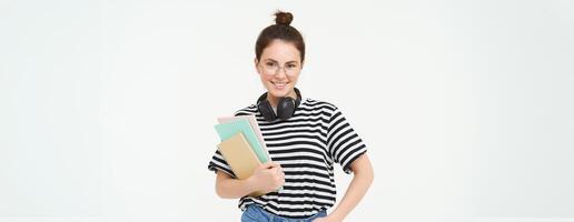 retrato do sorridente, confiante jovem mulher, segurando notas, cadernos dentro dela mãos, indo para faculdade, aluna posando contra branco fundo foto