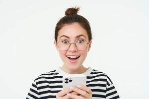 imagem do jovem mulher dentro copos, usando dela Móvel telefone, em pé com Smartphone e sorridente, em pé sobre branco fundo foto