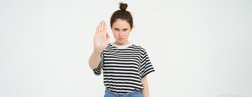 imagem do sério e confiante jovem mulher, mostra Pare sinal, tabu gesto, proibir alguma coisa ruim, em pé sobre branco fundo foto