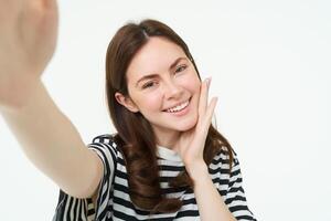 estilo de vida e pessoas conceito. jovem despreocupado mulher, sorridente enquanto levando selfie em Smartphone, posando para foto, em pé sobre branco fundo foto