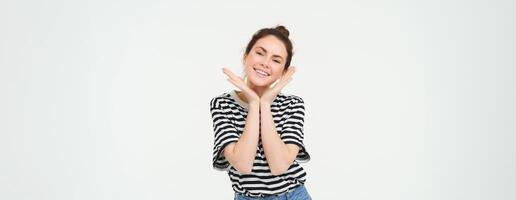 bem estar e mulheres conceito. retrato do jovem mulher com fofa face, detém mãos perto cabeça e sorrisos, isolado contra branco fundo foto