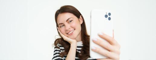 retrato do jovem mulher levando selfies em Smartphone, posando para foto,. usando Móvel telefone aplicativo para levando engraçado e fofa fotos, isolado em branco fundo foto