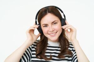 fechar acima retrato do fofa jovem mulher, sorridente, colocando em fones de ouvido, ouvindo para música dentro fones de ouvido, tentando em Novo fone de ouvido, branco fundo foto