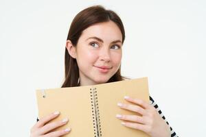 retrato do jovem mulher faz notas dentro dela planejador, escreve dentro diário, Verificações dela cronograma dentro caderno, segurando organizador dentro mãos, carrinhos sobre branco fundo foto