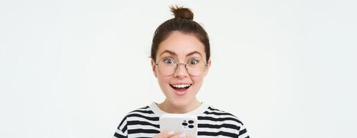 imagem do jovem mulher dentro copos, usando dela Móvel telefone, em pé com Smartphone e sorridente, em pé sobre branco fundo foto