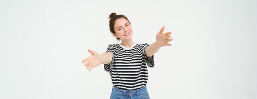 retrato do sorridente jovem mulher alcançando dela mãos, abraçando você, quer para abraçar, alongamento braços para receber, levar smth, em pé sobre branco fundo foto