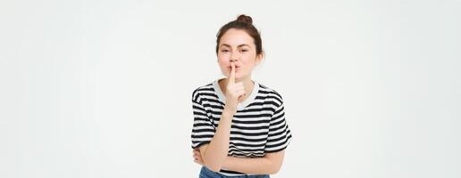 retrato do fofa menina mantém uma segredo, cala a boca, shhh gesto, prensas dedo para lábios, bisbilhotice, carrinhos sobre branco fundo foto