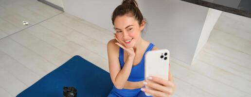 retrato do jovem estilo ginástica menina fazendo exercite-se a partir de lar, levando selfie e vídeo para social meios de comunicação, Academia instrutor registros dela Treinamento sessão dentro de casa foto