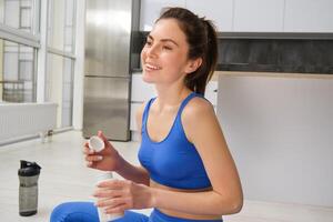 retrato do lindo e saudável ginástica mulher, levando vitaminas, dietético suplementos para músculos e ossos, fazendo exercite-se Treinamento às casa foto