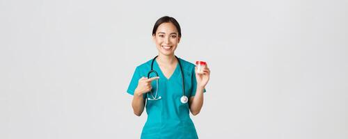 cuidados de saúde trabalhadores, impedindo vírus, quarentena campanha conceito. sorridente bonita ásia fêmea médico, enfermeira dentro esfrega mostrar vitaminas e apontando às pílulas, recomendar medicamento, branco fundo foto