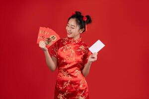 feliz ásia mulher vestindo vermelho qipao vestir segurando crédito cartão e Angpao ou vermelho pacote monetário presente isolado em vermelho fundo. foto