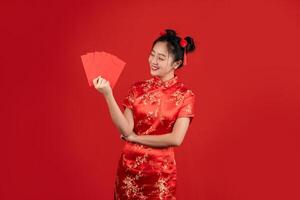 ásia mulher vestindo vermelho cheongsam em vermelho fundo. ela é segurando uma vermelho envelope. foto