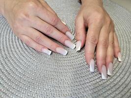 lindo fêmea mãos com delicado manicure em a fundo do uma cinzento guardanapo. mulheres unhas. foto