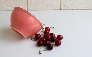 uma cereja com gotas do água mentiras em a branco cozinha mesa Próximo para uma Rosa tigela. rústico fruta fundo. foto