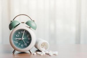 a alarme relógio com uma branco plástico garrafa contendo remédio em a mesa para Tempo gestão e cuidados de saúde conceito foto