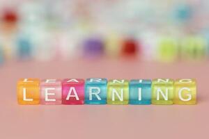 a palavra Aprendendo formado com multicolorido cubos em uma Rosa fundo foto