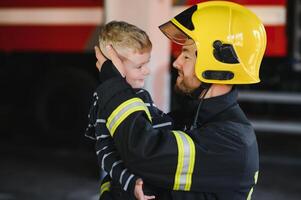 sujo bombeiro dentro uniforme segurando pequeno salvou Garoto em pé em Preto fundo. foto
