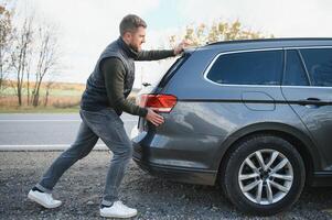 homem empurrando uma quebrado carro baixa a Rocha estrada foto