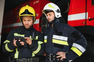 retrato do dois bombeiros dentro fogo brigando Operação, bombeiro dentro protetora roupas e capacete usando tábua computador dentro açao brigando foto