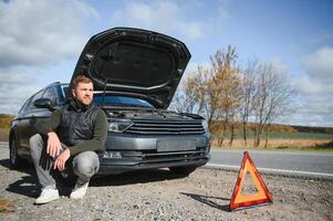 bonito jovem homem com dele carro quebrado baixa de a beira da estrada foto