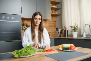 feliz sorridente fofa mulher é preparando uma fresco saudável vegano salada com muitos legumes dentro a cozinha às casa e tentando uma Novo receita foto