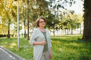 Senior mulher caminhando dentro a parque dentro verão. foto