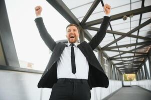 homem de negocios sorridente e levantando dele punho dentro a ar, com escritório construção fundo - o negócio sucesso, conquista, e ganhar conceitos foto