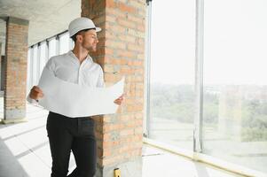 retrato do a arquiteto construtor estudando disposição plano do a quartos, sério Civil engenheiro trabalhando com documentos em construção site, construção e casa renovação, profissional capataz às trabalhar. foto