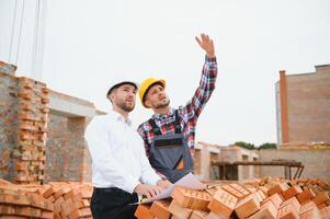 engenheiro arquiteto com Difícil chapéu e segurança colete trabalhando juntos dentro equipe em principal construção local foto