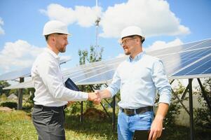 dois pessoas tendo uma tremendo mãos contra solar painel depois de a conclusão do a acordo dentro a renovável energia foto