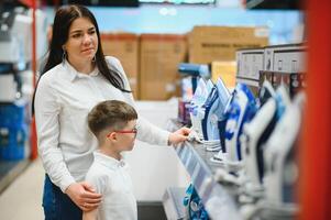 mulher com filho escolhendo elétrico ferro dentro eletrônicos loja foto