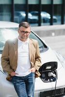 casual homem perto elétrico carro esperando para a terminar do a bateria cobrando processo. foto