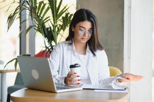 sorridente menina aluna estude conectados com skype professor, feliz jovem mulher aprender língua ouço palestra Assistir webinar escrever notas Veja às computador portátil sentar dentro cafeteria, distante Educação foto