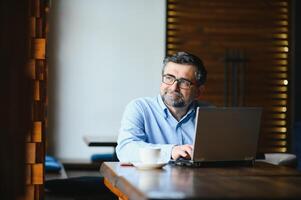 negócios, tecnologia e pessoas conceito , Senior homem de negocios com computador portátil computador bebendo café às moderno cafeteria. foto